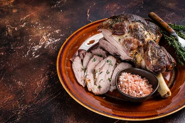 Deurstickers BBQ Roast Lamb mutton leg sliced on a rustic plate. Dark background. Top view. Copy space © Vladimir