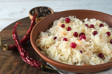 Sauerkraut with cranberries in a brown clay plate on a wooden background. Fermented vegetables. Super product for proper nutrition.