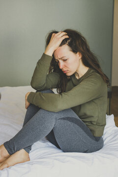 Sad thoughtful worried brunette girl looking away sit in bed at home interior. Feeling depressed doubtful, psychological problem, thinking regret about mistake, unexpected pregnancy concept. Vertical