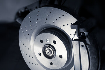 Installation of new perforated brake discs and pads on a modern auto in a car workshop. Blur effect.