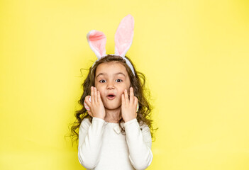 Obraz na płótnie Canvas A charming cheerful girl with a happy surprised smile touches her cheeks and holds Easter eggs in her hands, expresses her love for you, wears fluffy ears, wearing a T-shirt. Happy moments. Easter and