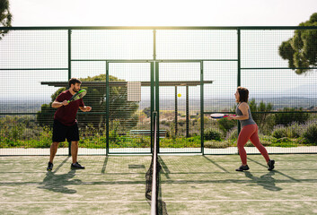 Two friends playing paddle tennis on a sunny day. Man and woman playing paddle tennis having fun