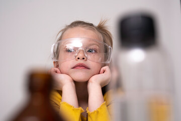 Laboratory, children's chemical experiments day 1 of 14. A dreaming blonde girl in plastic goggles,...