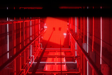 Lift shaft in a residential building. Elevator corridor in the building lit by red elumination. Futuristic elevator shaft is located in a high tower. Abstract, background. Bottom view © polack