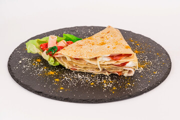 Homemade folded crepe with chopped cheese, ham and ketchup on black round plate isolated on white background