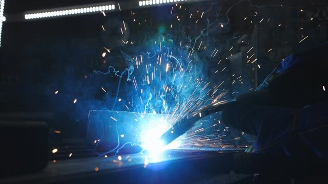 Close-up slow motion welding of a metal part in an auto repair shop.