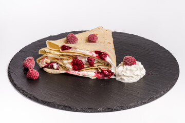 Homemade folded crepe with raspberries and whipped cream on black round plate isolated on white background