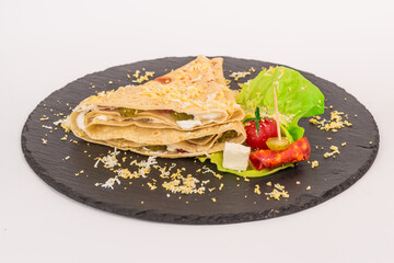 Homemade folded crepe with chopped eggs on top, cucumbers and salad on black round plate isolated on white background