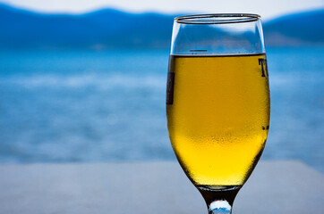 a glass of cold beer in front of a blurred view of the sea and mountains in the background,  enjoying a beer by the calm sea