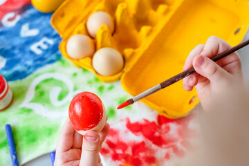 close up child paints Easter eggs red. paint stains on the background
