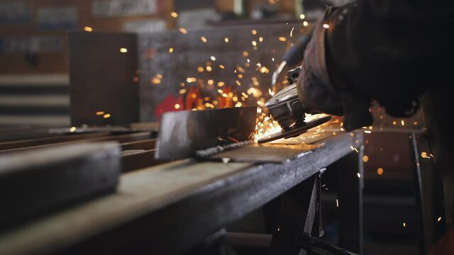 Sparks fly away from the grinder in the hands of a mechanic grinding a metal part in an auto repair shop