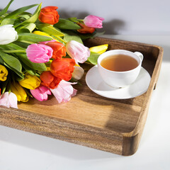 Fototapeta na wymiar A bouquet of multicolored tulips and a cup of tea are on a tray on the table