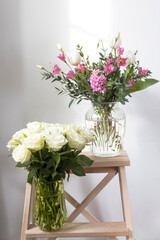 A minimalistic bouquet of white tulips, pink eustoma, hyacinth, eucalyptus in a fluted glass vase on a white panel of an artificial fireplace.