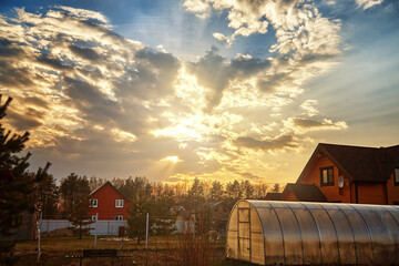 Beautiful sunset and clouds with sun rays in evening over small village house. Country living concept. Rural landscape.