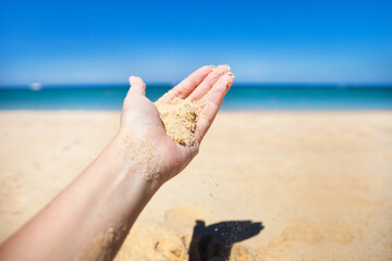 Sand falls from the girl's hand against the background of the sea shore on a sunny day.