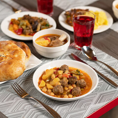 Vegetable stew or tomato soup with meatballs. Set lunch served on restaurant table with fork and spoon, knife, cutlery on it. Nutritious dinner. Copy space. Soft focus. Square format for web banner.