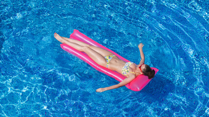 young brunette woman tanning on pink inflatable mattress in swimming pool