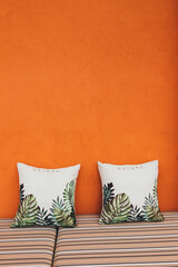 Two pillows against the background of an orange textured wall with a striped sofa in a modern cafe