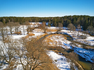 Early spring landscape with melting snow and meadow. Forest and Isloch creek in sunny march april day.