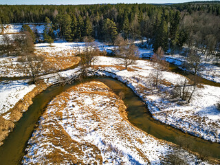 Early spring landscape with melting snow and thawed patches in meadow. Forest and Isloch creek in sunny march day.