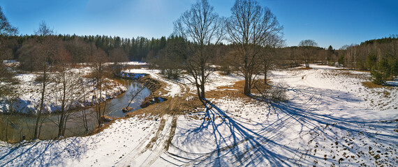 Early spring landscape with melting snow and thawed patches in meadow. Forest and Isloch creek in sunny march