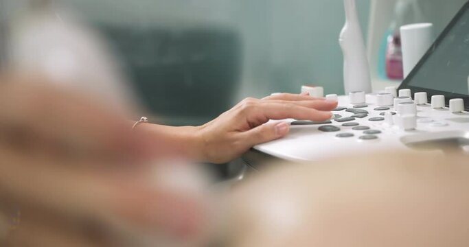Close up cropped image of female doctor obstetrician, pushing buttons on a control panel performing ultrasound sonogram procedure for pregnant woman
