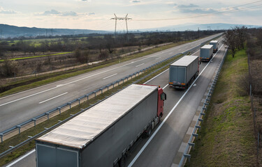Convoy of Big Transportation trucks departing on a country highway under a sunset sky. Business...