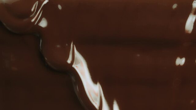 Close-up macro shot hot melted liquid chocolate flows, flowing molten chocolate or dark caramel stream. Cooking handmade chocolate dessert and candies. Confectionery. Pouring chocolate waves
