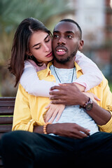 beautiful multi-ethnic couple in love embracing each other sitting on the bench of a city park, multicolored.