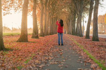 Teen girl taking photos of beautiful autumn trees with smartphone