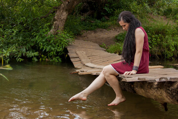 Girl sitting on a wooden bridge over the river and reading a book