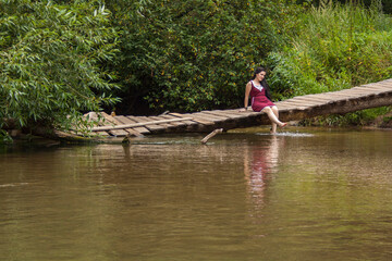 Fototapeta na wymiar Girl sitting on a wooden bridge over the river and reading a book
