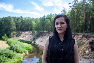A girl stands by a stream in the forest flowing through a ravine