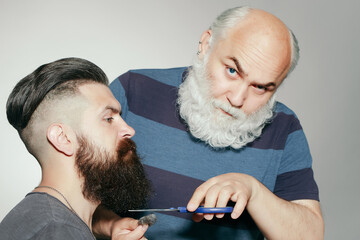 Old and young bearded men with long beard on grey background. Hairdresser with scissors cutting...