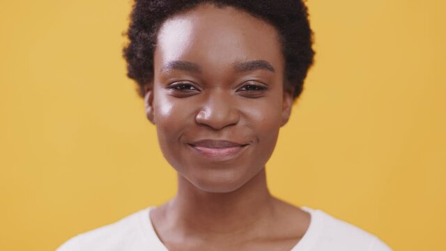 Portrait of tricky african american lady looking and camera and smiling, orange studio background, slow motion