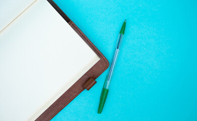  Top view photo of closed brown notebook and ball-point pen over turquoise blue background