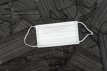White surgical mask with a background of scattered black surgical masks. Top view