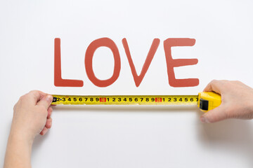Hands measuring with measuring tape word LOVE on wall. Abstract concept.