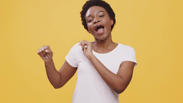 Disco fun. Happy carefree african american lady with cut curly hair dancing and singing over yellow studio background