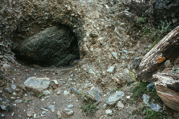 Beautiful nature background with big black stone in hole in mountain. Minimalist mountain landscape with large black boulder in dark rock hollow close-up. Atmospheric nature minimalism in mountains.