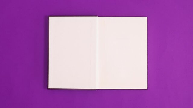 Purple vintage hardcover book appear and open with copy space on purple background. Stop motion flat lay