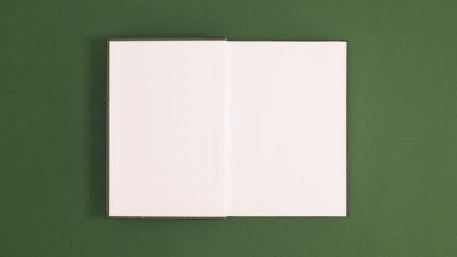 Green vintage hardcover book appear and open with copy space on green background. Stop motion flat lay