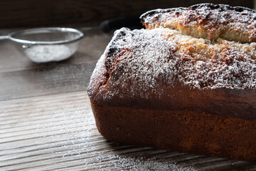 A freshly baked loaf of banana nut bread dusted with powder sugar sitting on a wood countertop