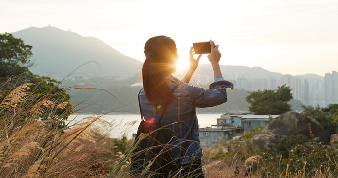 Woman uses mobile phone to take photos at sunset