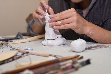 artisan hands molding a sculpture in clay and molding paste, on a table with several molding tools and brushes