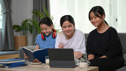 Fototapeta premium Three young girls watching something funny on digital tablet while siting together on sofa in living room.