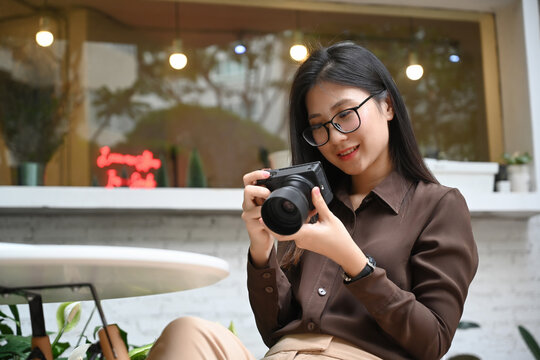 Happy young woman sitting in cafe and checking photo in her camera.