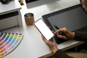 Cropped shot of female graphic designer sitting at her workplace and using smart phone.