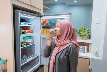 muslim woman taking some fruit out of the fridge and eat, dieting concept