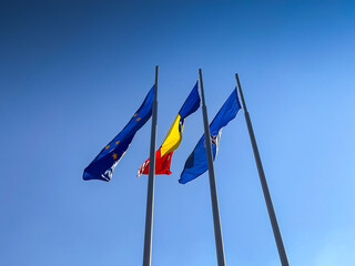 Flags of Romania, European Union and NATO winding on a blue sky background